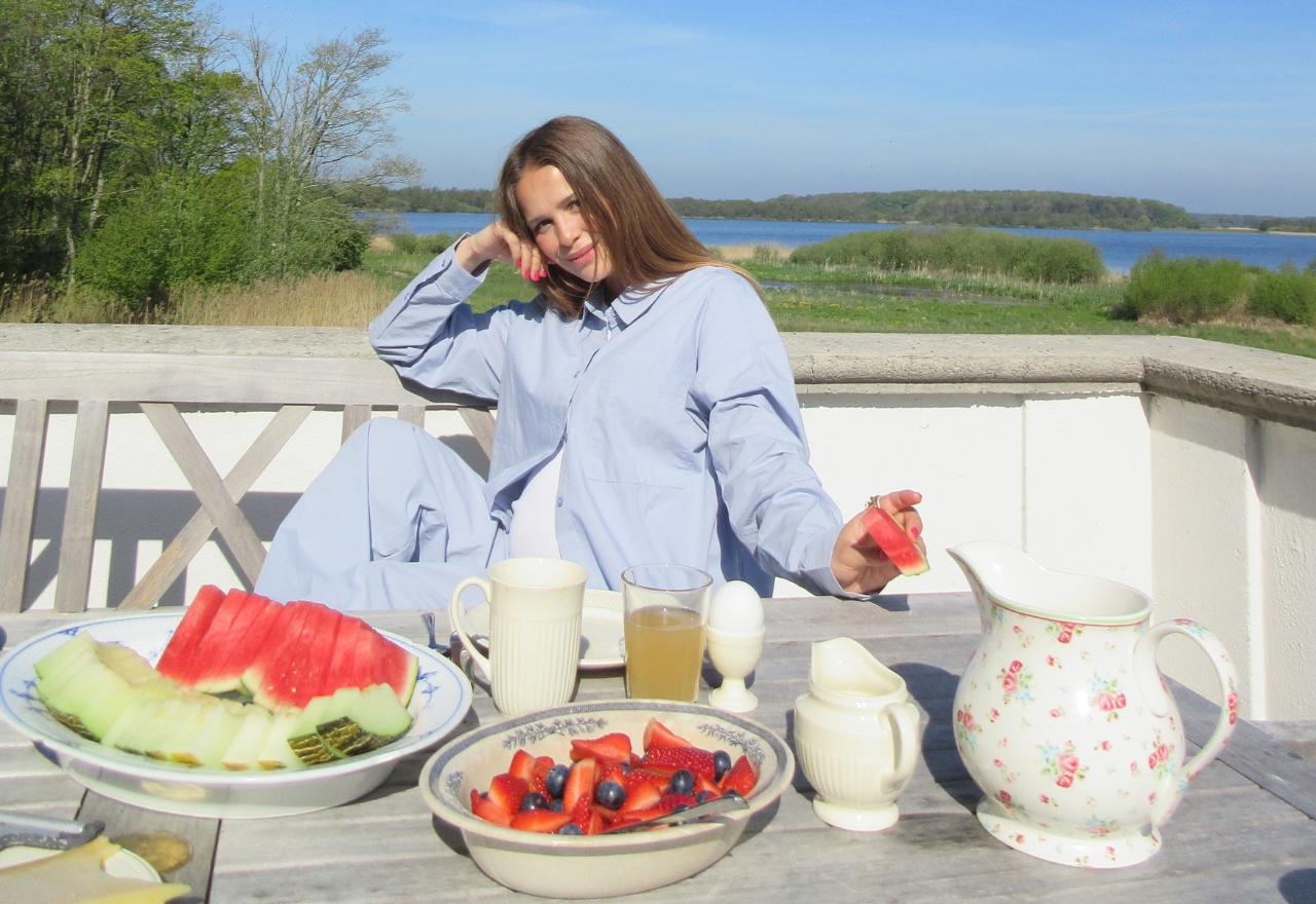 Kvinde på altan iført blå skjorte sidder med vandmelon i hånden